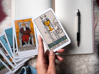 an image of a person holding the ace of cups card against the background of a journal