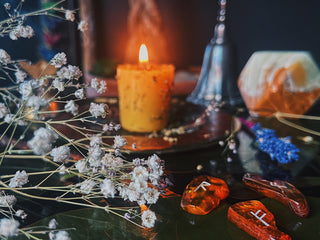 Lit glowing spell candle, carved with intentions, dressed in oil for manifesting surrounded by, dried babies breath and amber runes