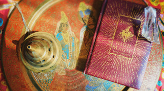 A still life tableau featuring a closed High Magic book with a chunk of energy-charged crystal perched on top, set beside ornate censers with incense burning on a brass plate, symbolizing the quiet anticipation before commencing a chaos magic ritual