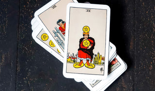 Rider-Waite tarot deck with the Four of Pentacles card on top, showing a figure clutching pentacles tightly. Other pentacle and sword cards are partially visible beneath on a dark surface.