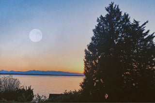 A picturesque sunset over the Pacific Northwest Sound reveals the Full Moon ascending over majestic mountains.