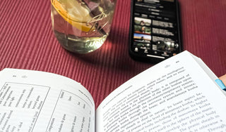 Open book on Ayurvedic philosophy and the koshas resting on a yoga mat, with a lemon water jar and smartphone nearby—symbolizing holistic study and mindful self-care.