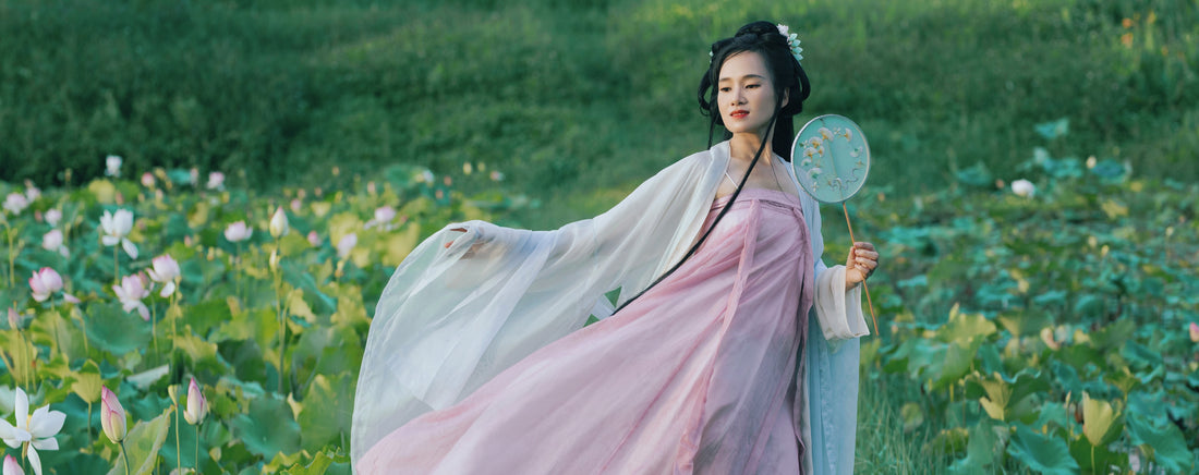 A woman dressed in traditional Chinese hanfu walking through a green field of flowers
