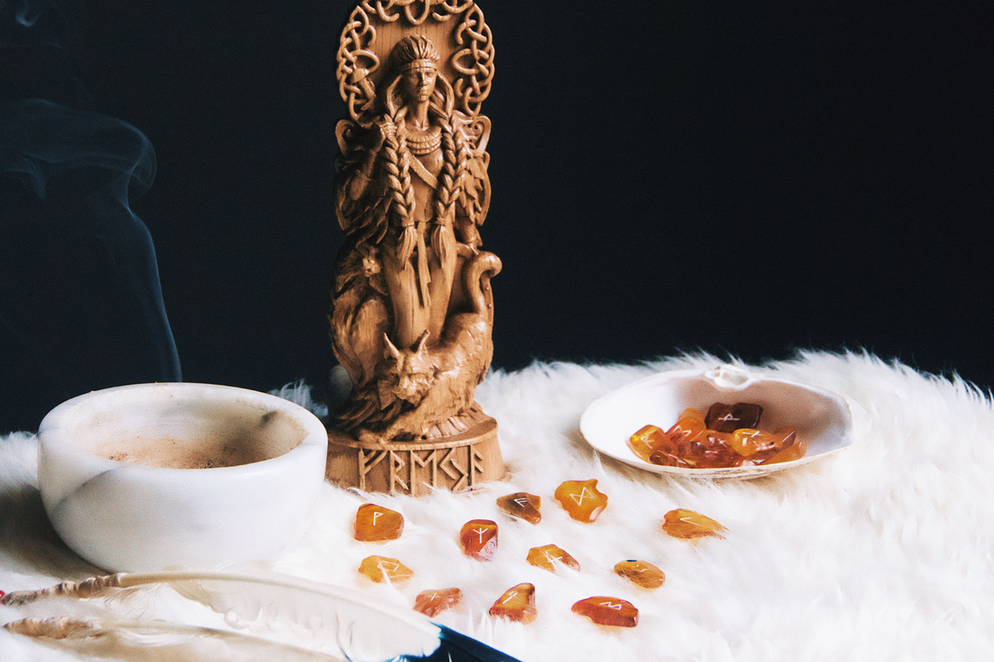 A wooden statue of Freyja overlooks baltic amber runes as incense burns in a marble bowl