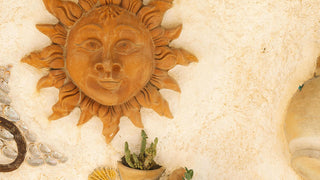 Sun face carving on a wall surrounded by shells and cacti, symbolizing Leo energy.