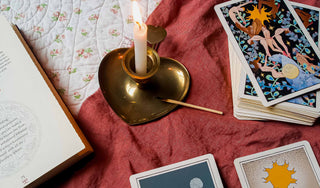 Flat lay of a Sagittarius Full Moon ritual setup with tarot cards, a lit candle in a brass heart-shaped holder, and an astrology book open on a quilt. A calming and mystical atmosphere for lunar reflection, tarot reading, and spiritual practice.