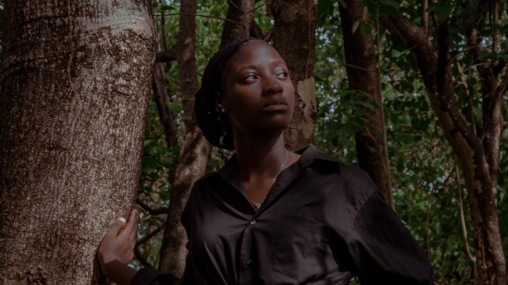 A beautiful African American woman walks in the forest in a dark black blouse as her hand touches a tree she is representing the mutable Earth sign of Virgo the maiden. 
