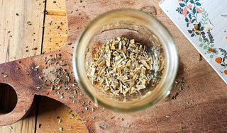 Overhead view of chopped mimosa bark in a glass jar on a wooden board—used in herbal formulation for emotional healing and tincture making.