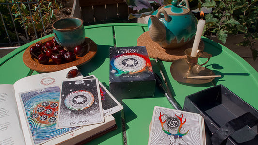 A tarot spread laid out on a green table with guidebooks, cherries, tea, and a burning candle, creating a serene setting for a reading session.