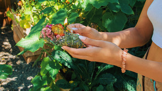 Person lighting a flower wand for an outdoor ritual, with a lush vegetable garden in the background; a perfect illustration of the Witch Tip: Rituals Reimagined - Take Your Incense & Smudge Sticks Outdoors.