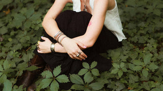 A person sitting cross-legged in a forest, surrounded by lush greenery.